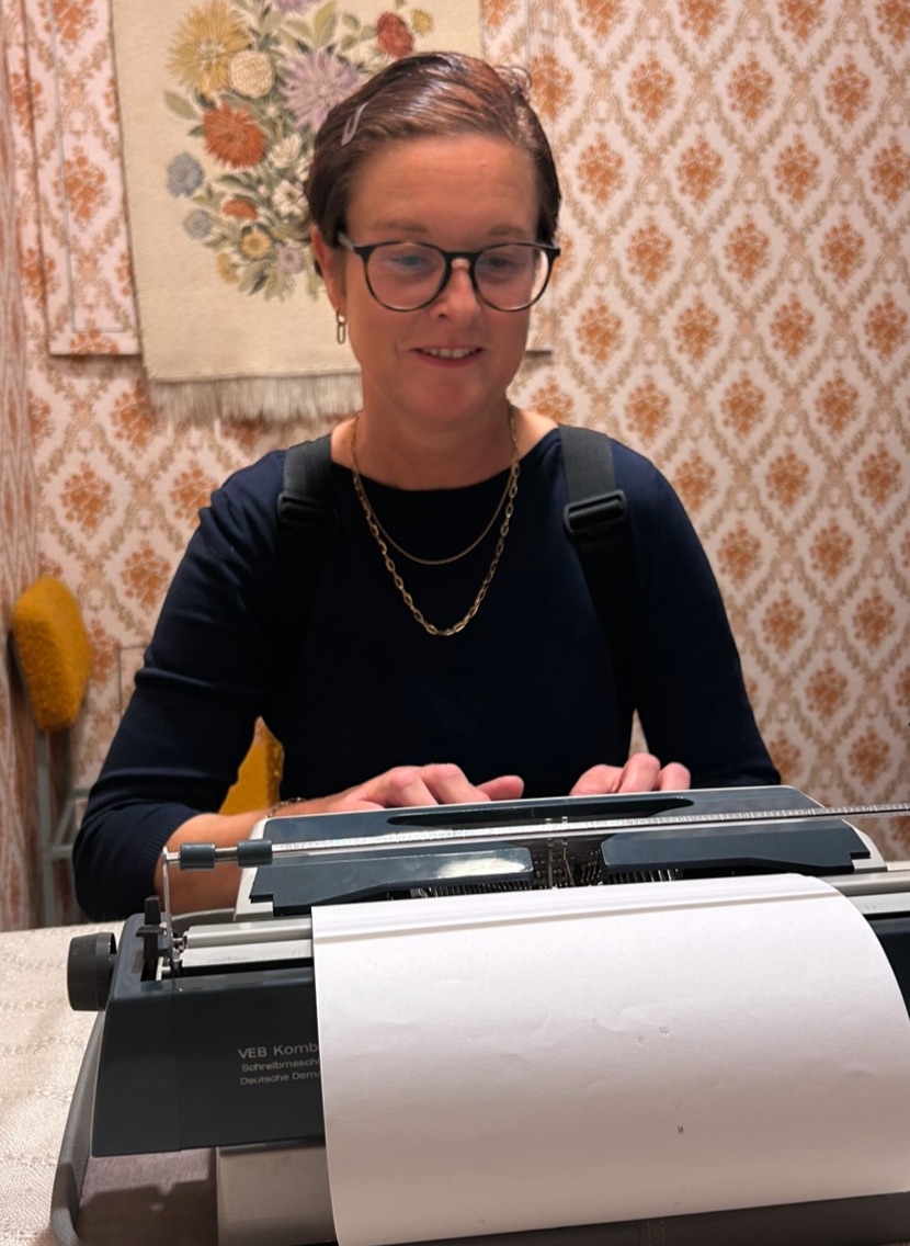 Die Frau sitzt hinter einer Schreibmaschine und man sieht ihre Finger über den Tasten.