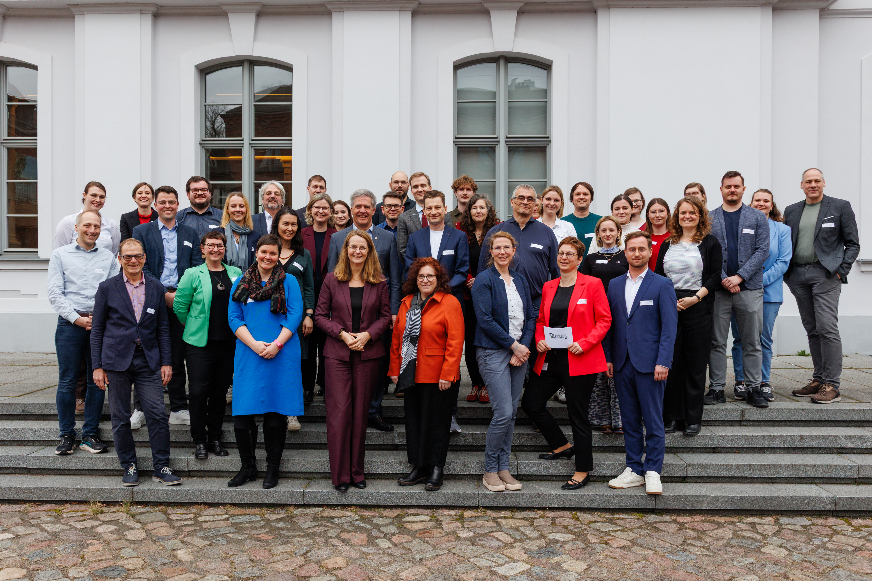 Gruppenfoto beim QLever-Auftakt von verschiedenen Menschen vor dem Unihauptgebäude