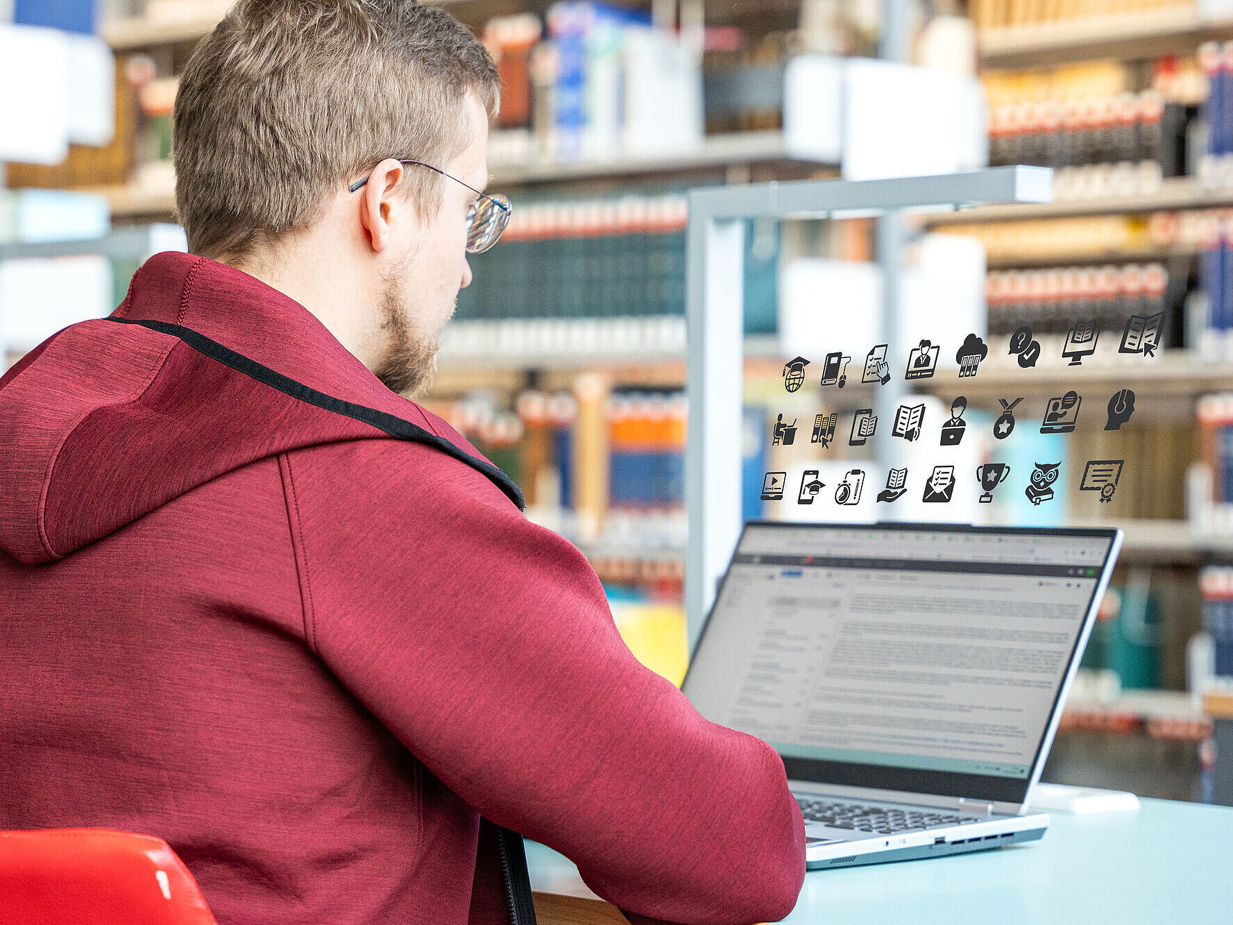 In einer Bibliothek sitzt ein Student vor seinem Laptop.