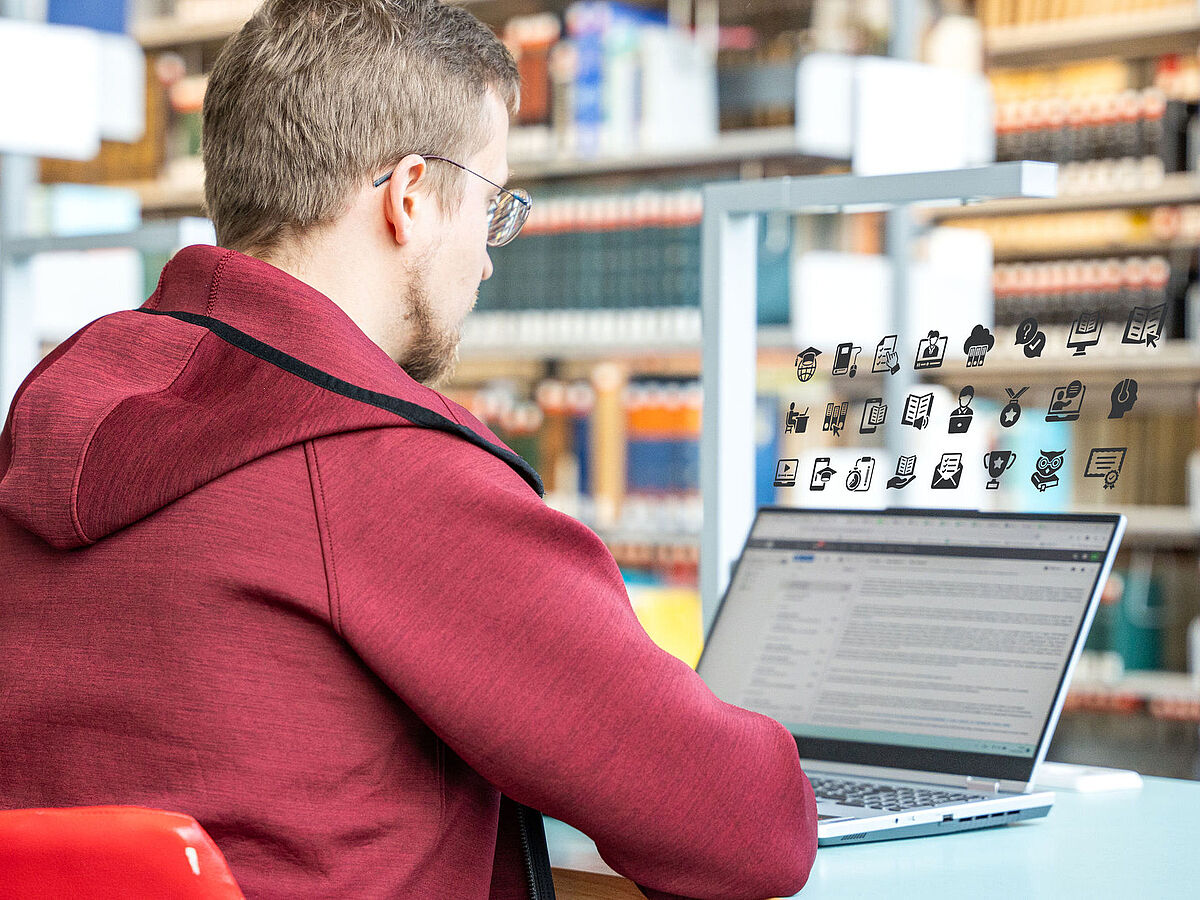 In einer Bibliothek sitzt ein Student vor seinem Laptop.