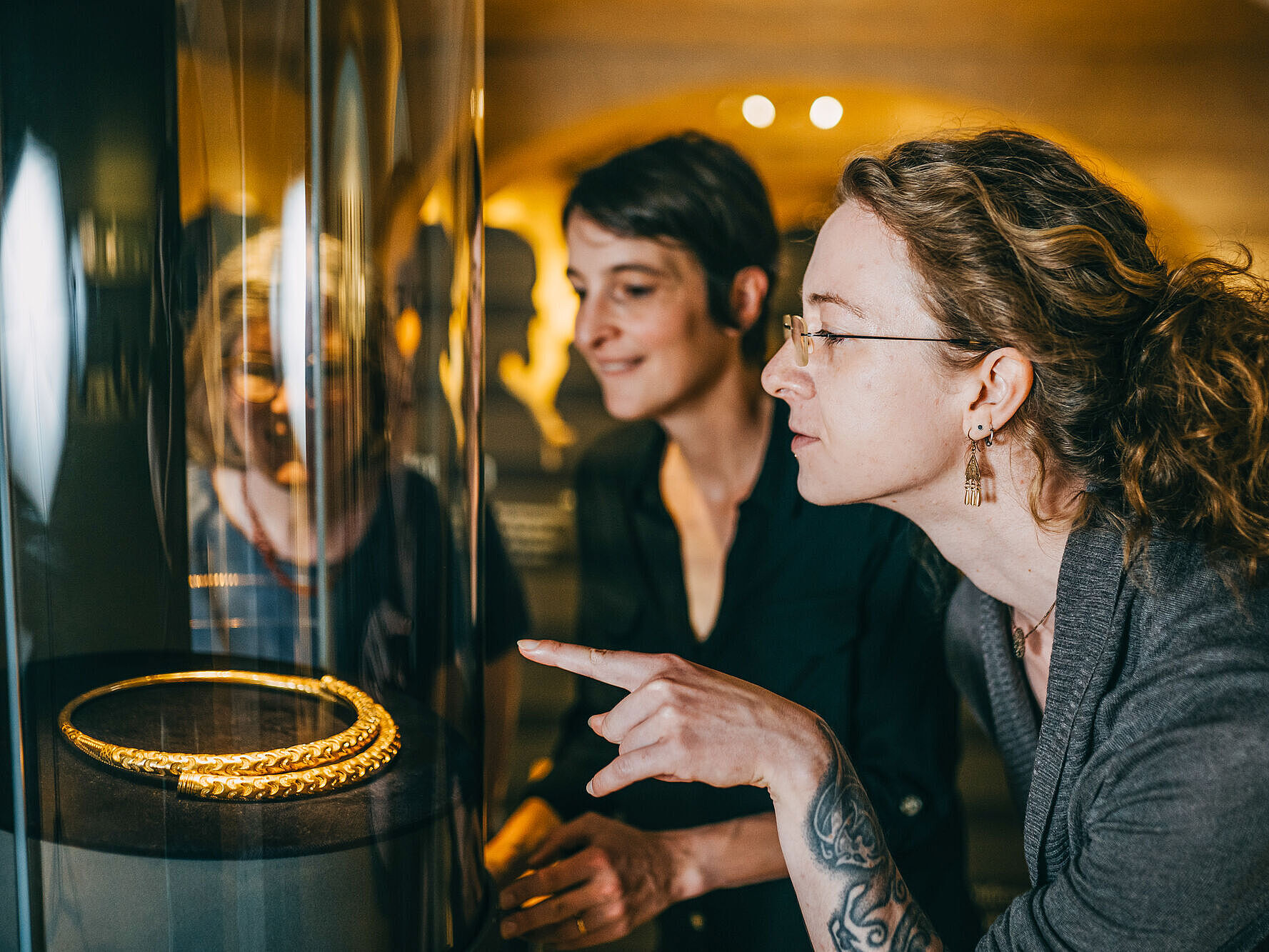 Symbolbild Besuch im Museum Zwei Personen schauen sich im Museum eine Vitrine mit einem goldenen Schmuckstück an.