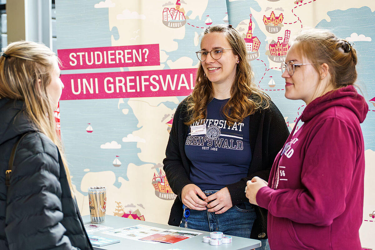 Zwei Campusspezialistinnen beraten eine Besucherin an den Hochschulinfotagen.