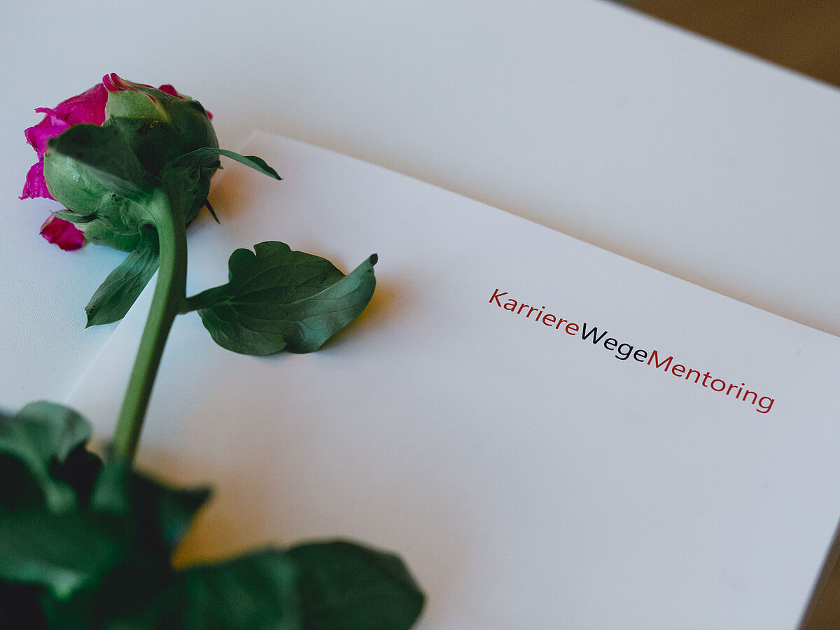 Auf einer weißen Karte liegt eine rote Rose.