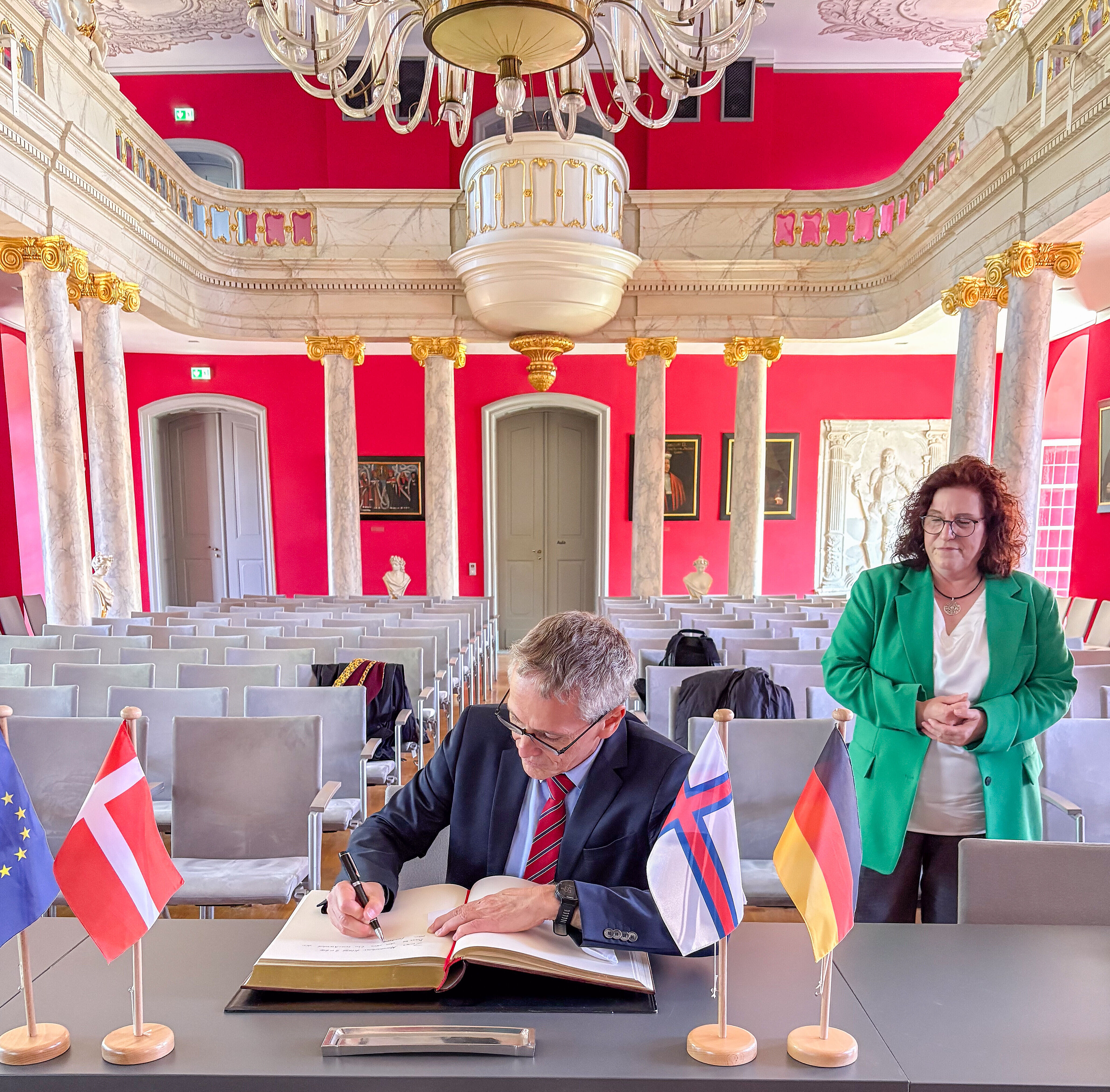 Besuch der dänischen Delegation während des 35. Nordischen Klangs: Der dänische Botschafter trägt sich in der Aula der Universität in das Goldene Buch ein. Schräg hinter ihm steht die Rektorin.
